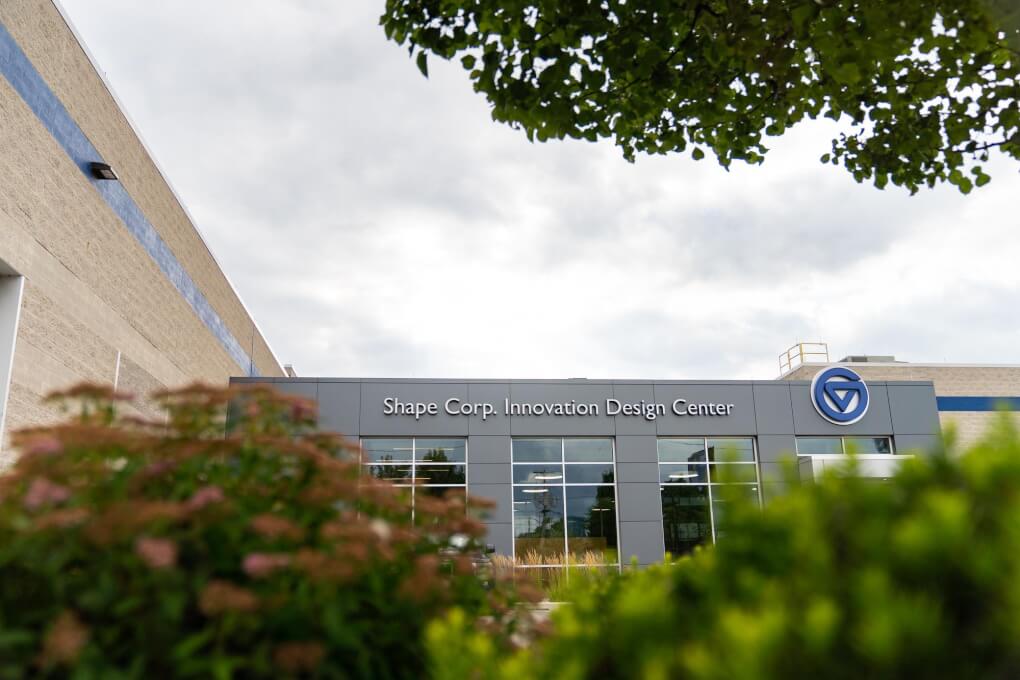 A building with the words 'Shape Corp Innovation Design Center' and the GVSU logo is pictured framed by bushes and trees.